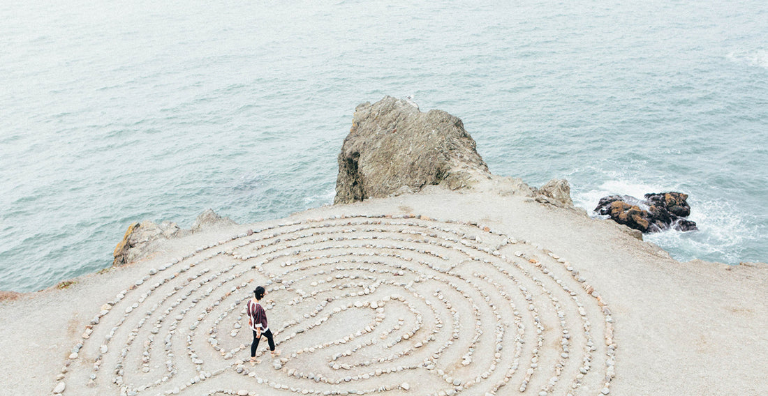 A person standing on a secluded beach, forming a circle of lines in the sand. 