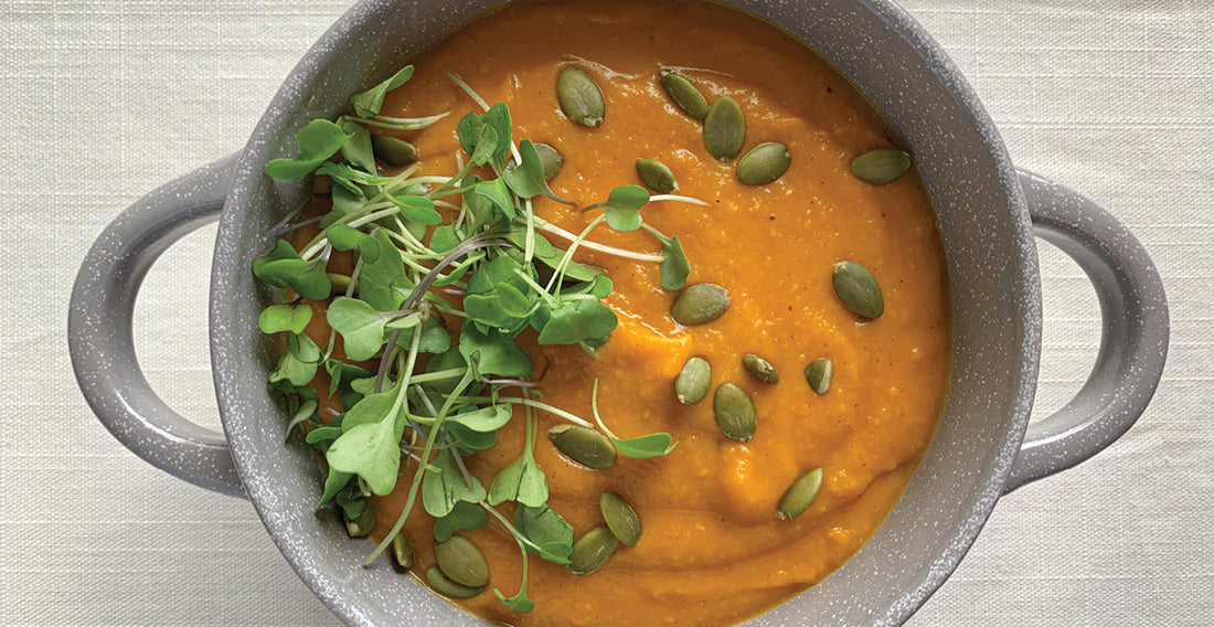 An image of golden blend butternut squash soup, garnished with some greens. 