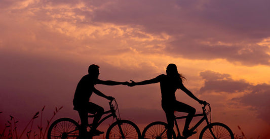 Two people holding hands as they bike together at sunset. 
