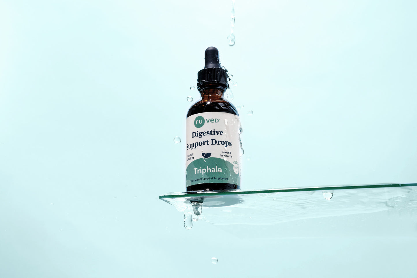 A bottle of ruved Triphala Digestive Support Drops with water falling on it. 